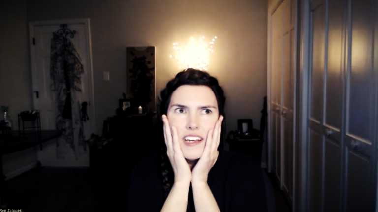 A clip of Ren Zatopek from a Hedge + Riders online class, her hands on her cheeks and eyes wide and she tells yet another weird story. Her dark hair is braided up and over her head. The room is dim, her t-shirt dark in contrast to her pale skin.